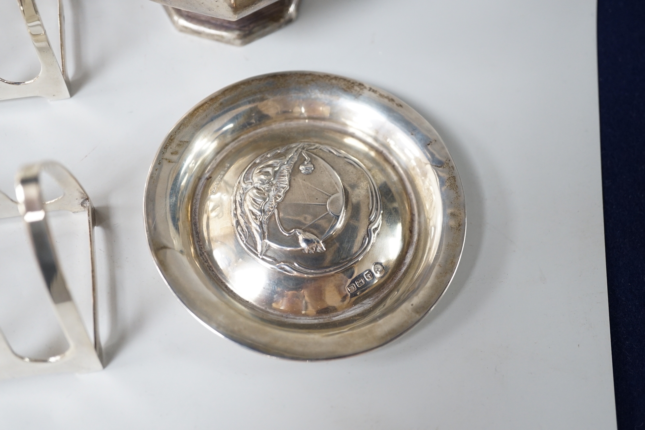 A George V octagonal silver caster, Sheffield 1932, 121 grams, a pair of Walker & Hall toast racks, Birmingham 1921, 101 grams and a trinket dish, decorated with waterlilies, Birmingham 1909, 18 grams